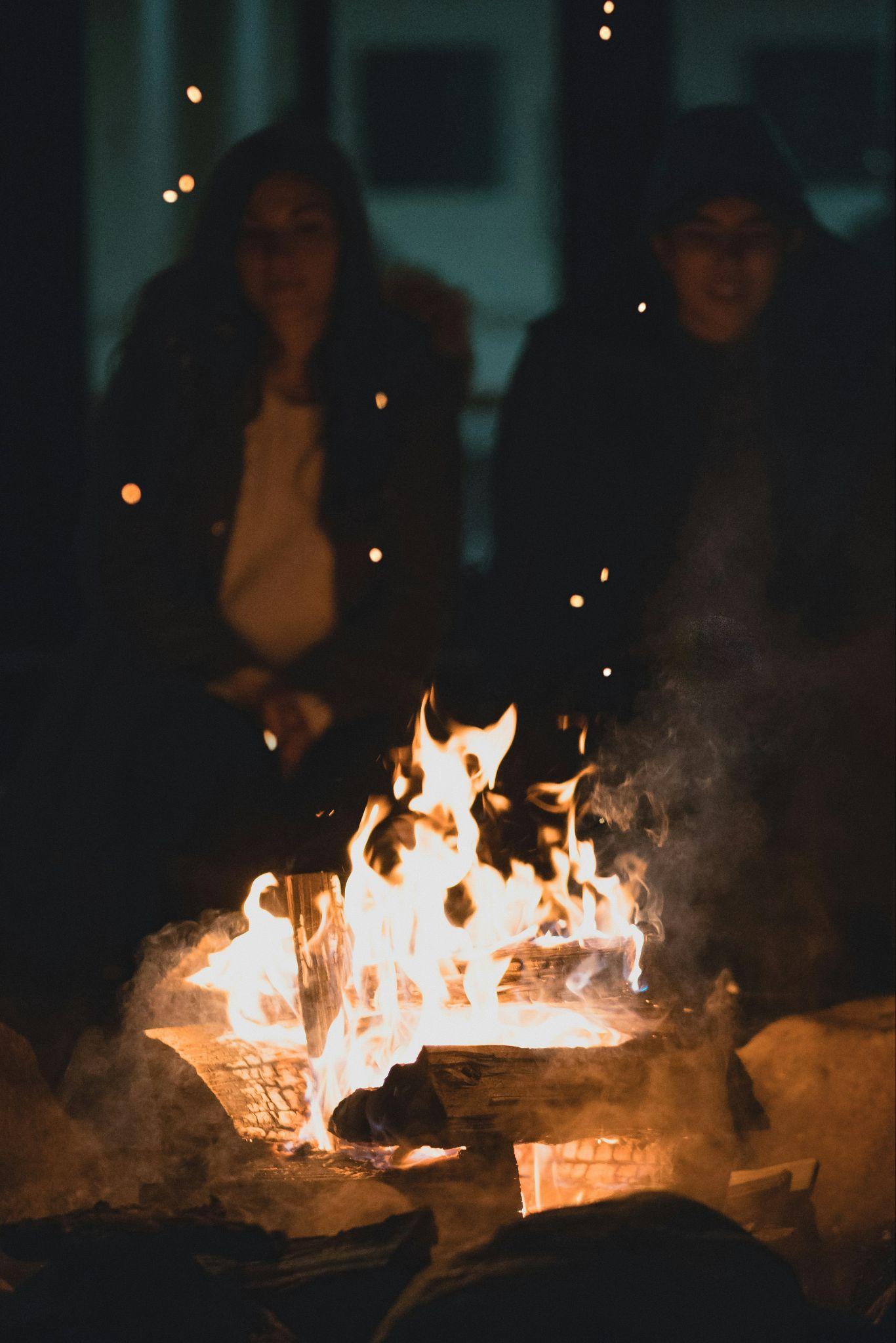 Two women gathered around a glowing campfire at dusk