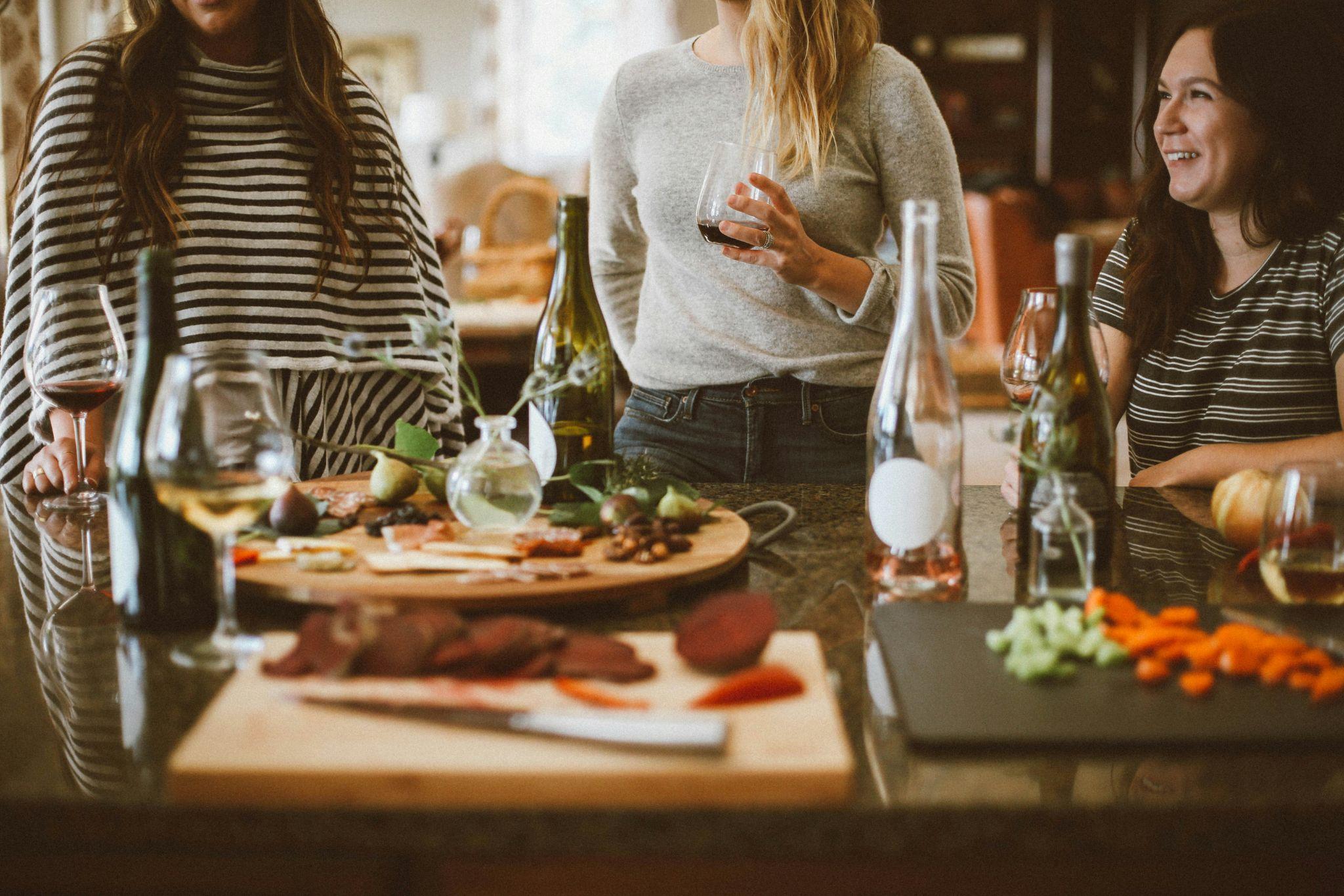 Women gathered around the kitchen island with wine and a cheese board